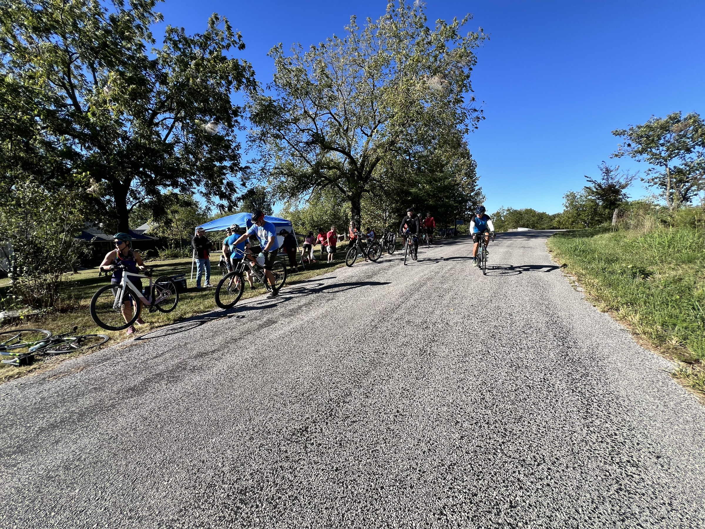 Pack of Country Miler riders on a country road with a tent visible on the left