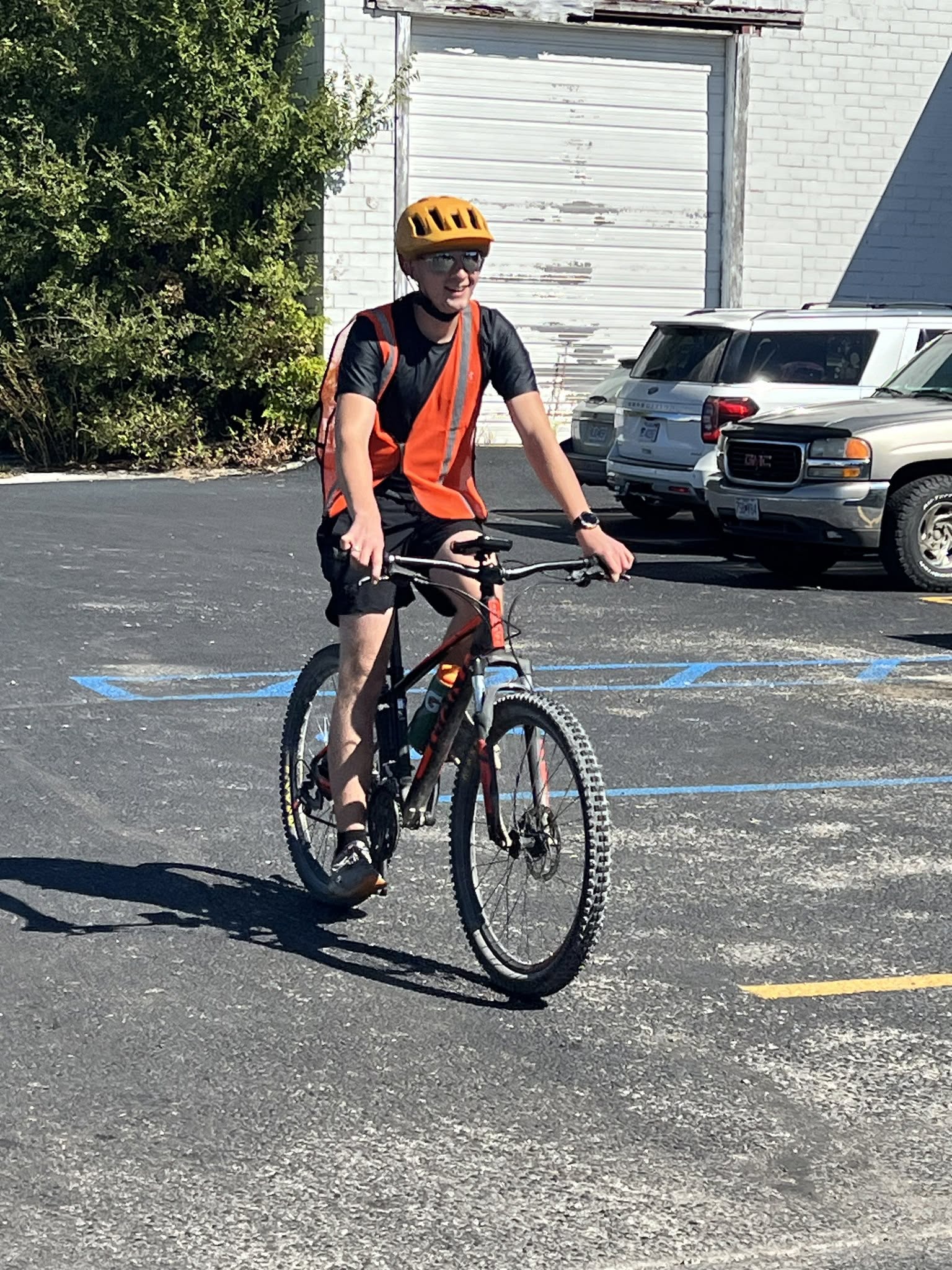 Smiling young mountain bike rider in an orange safety vest and yellow helmet